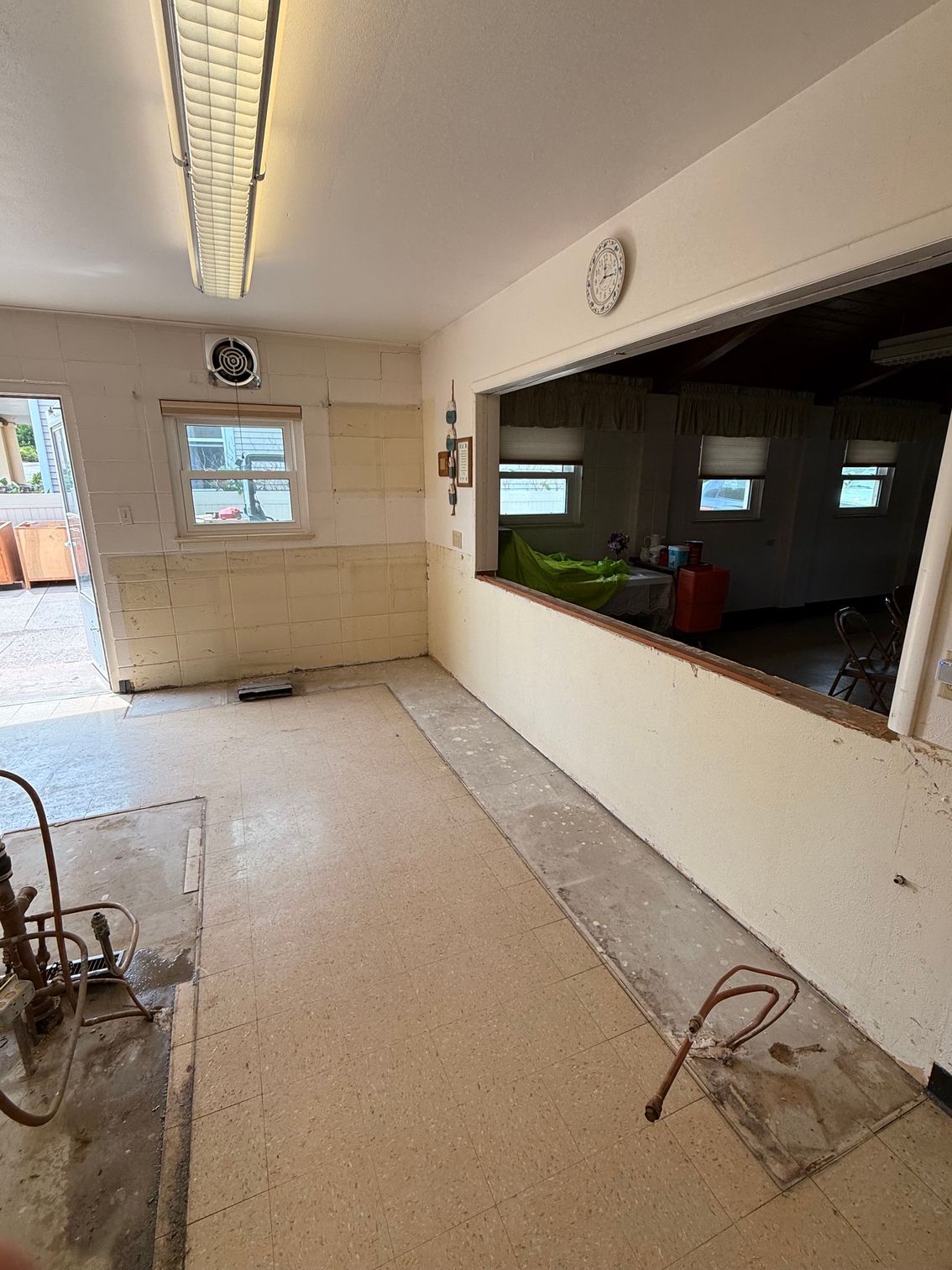 Empty tiled room with fluorescent lights, serving window, and small back window.