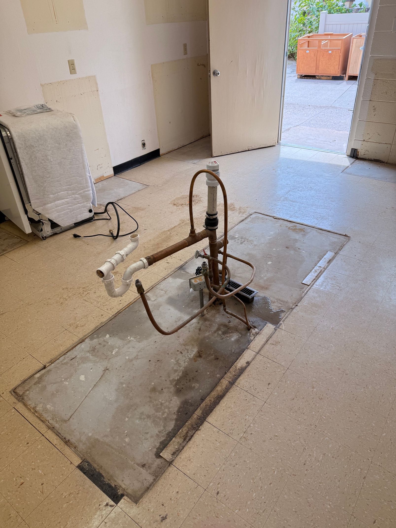 Floor-mounted water pump in a concrete room with hoses and a doorway leading outside.