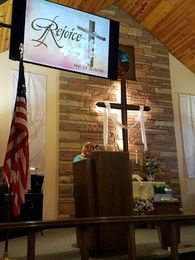 Woman speaking at a church podium with a cross and screen displaying 