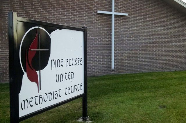 Sign for Pine Bluffs United Methodist Church with a cross on a brick building in the background.