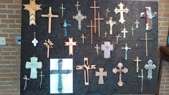 Display of various crosses on a dark background, some ornate, others simple, on a brick wall.