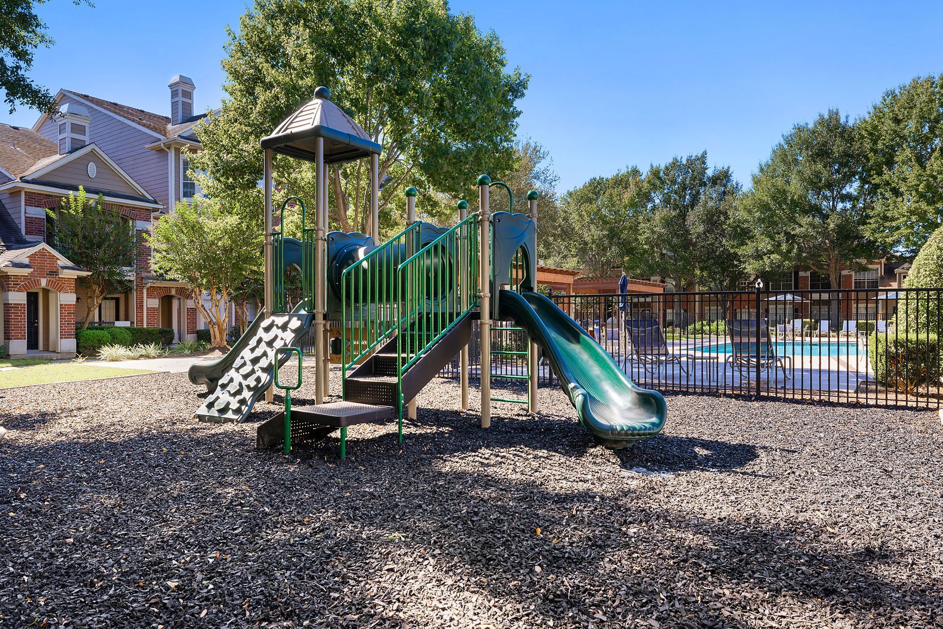 Outdoor playground with green slides and climbing structures in a multifamily community courtyard.