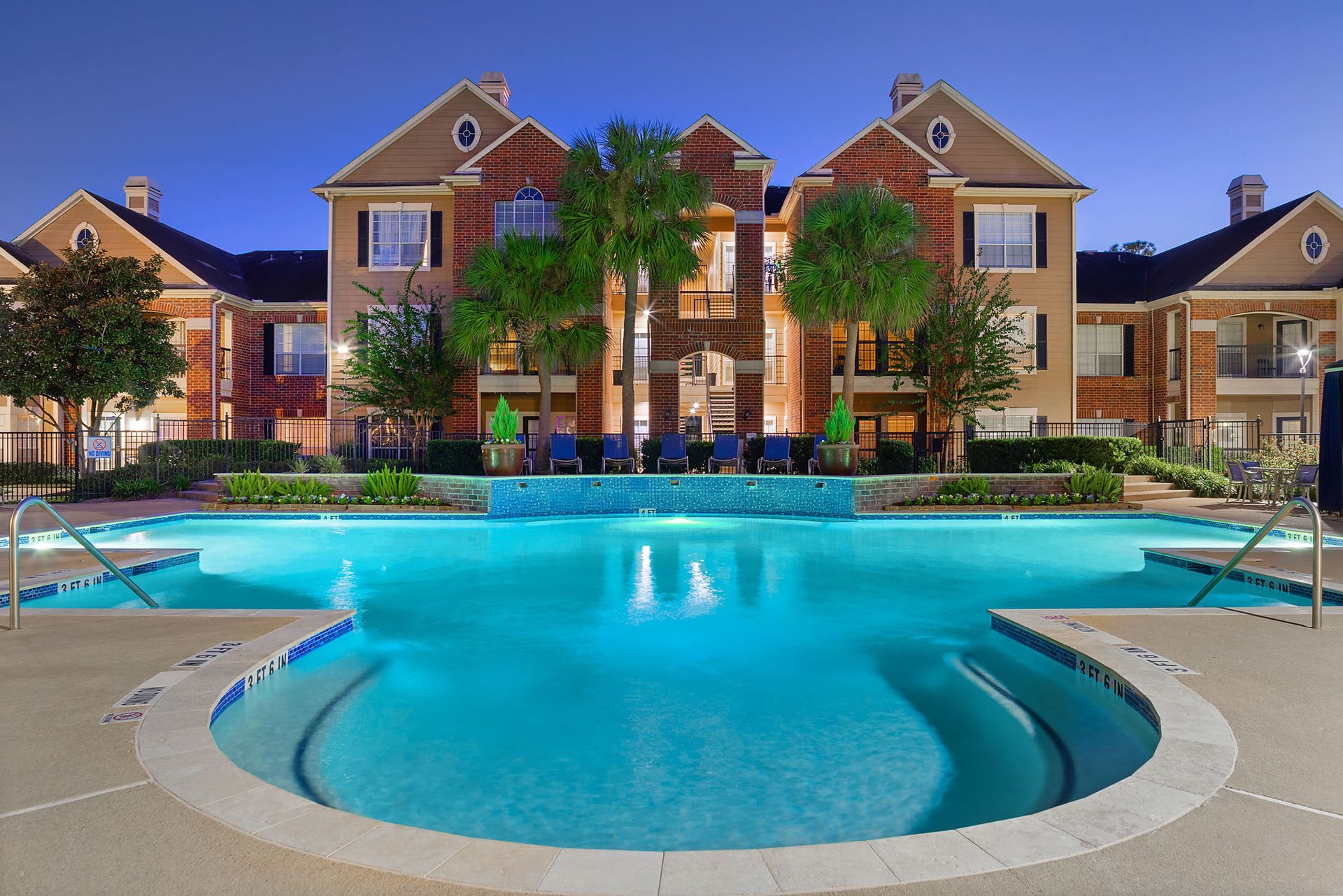 Outdoor pool at an apartment complex with lounge chairs and palm trees at dusk.