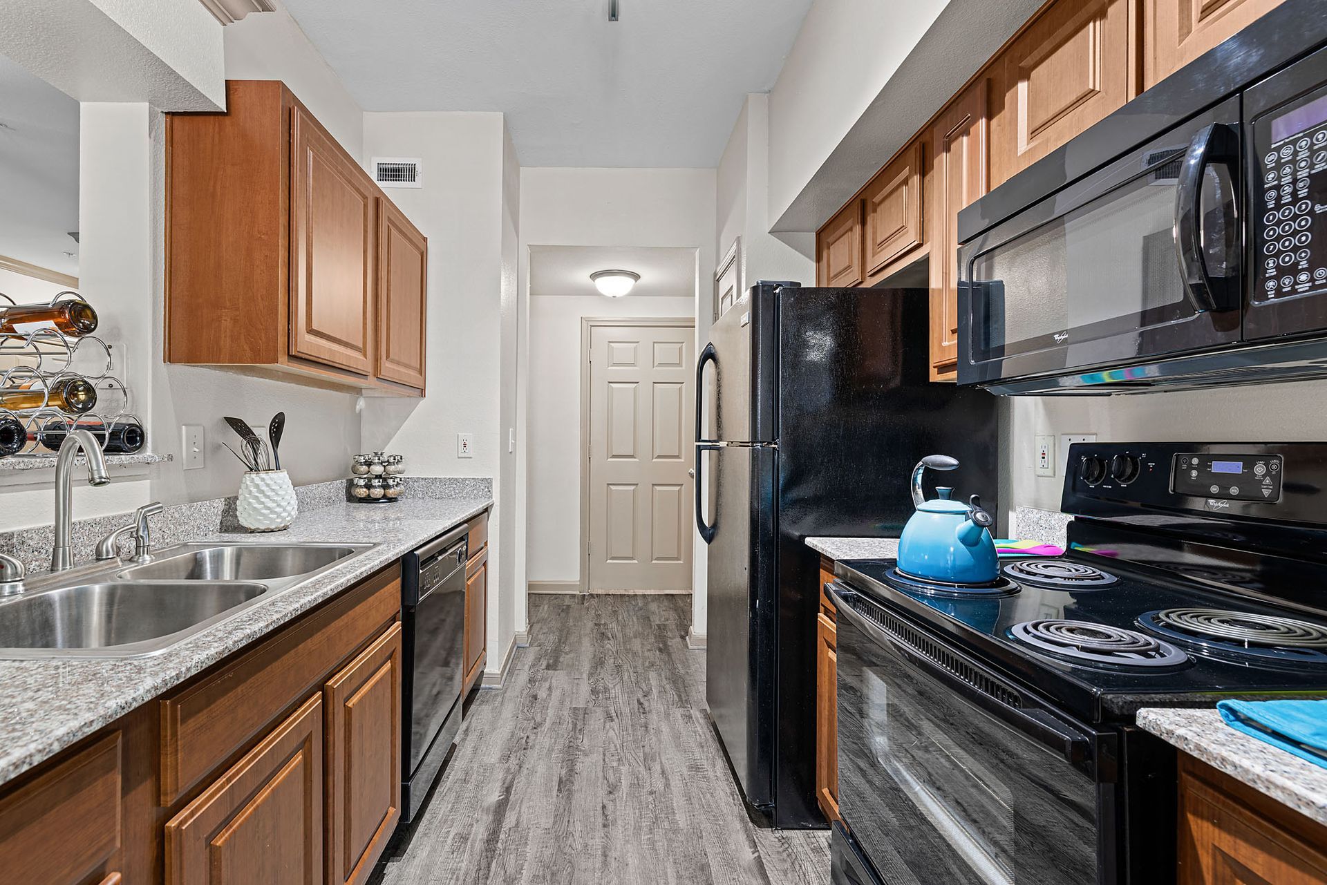 Galley-style apartment kitchen with wooden cabinets, granite countertops, and black appliances.
