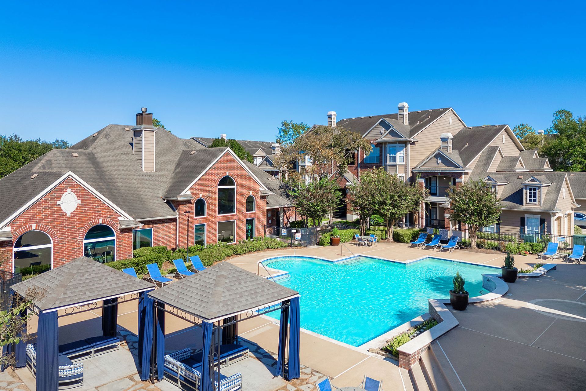 Aerial view of a large outdoor pool in a multifamily community with cabanas and surrounding buildings.