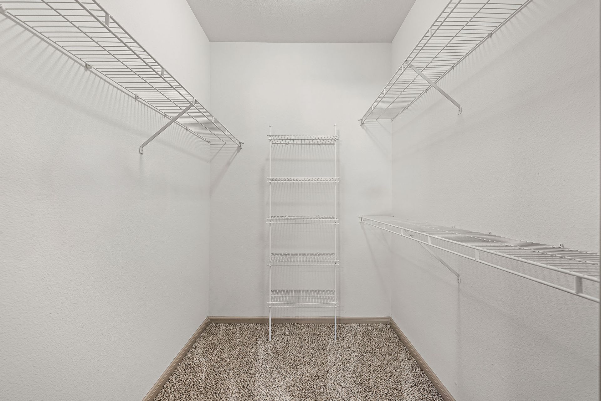 White walk-in closet with wire shelving along the walls and a freestanding rack in the center.