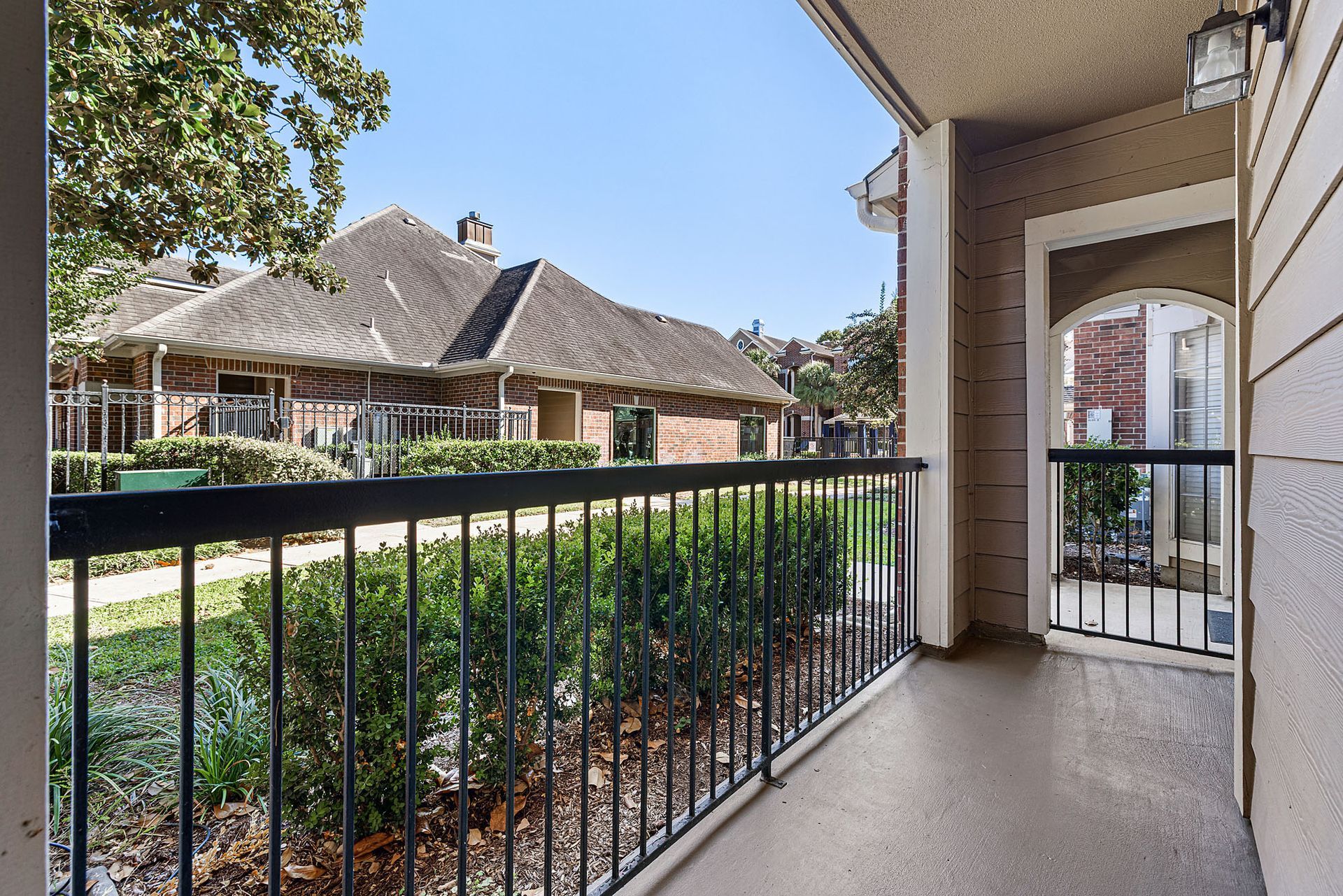 Balcony view of a brick apartment building, railing, and landscaped courtyard.
