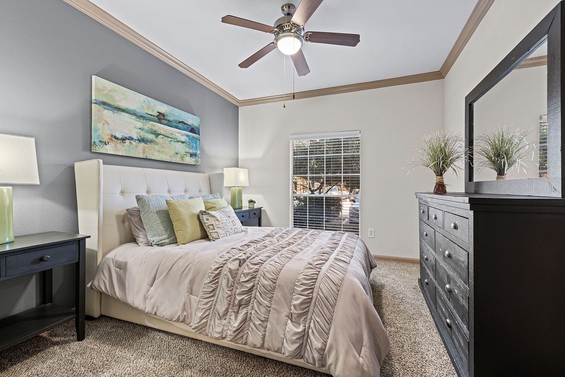 Bedroom featuring a white upholstered headboard, dark wood dresser, two nightstands, ceiling fan, and window with blinds.