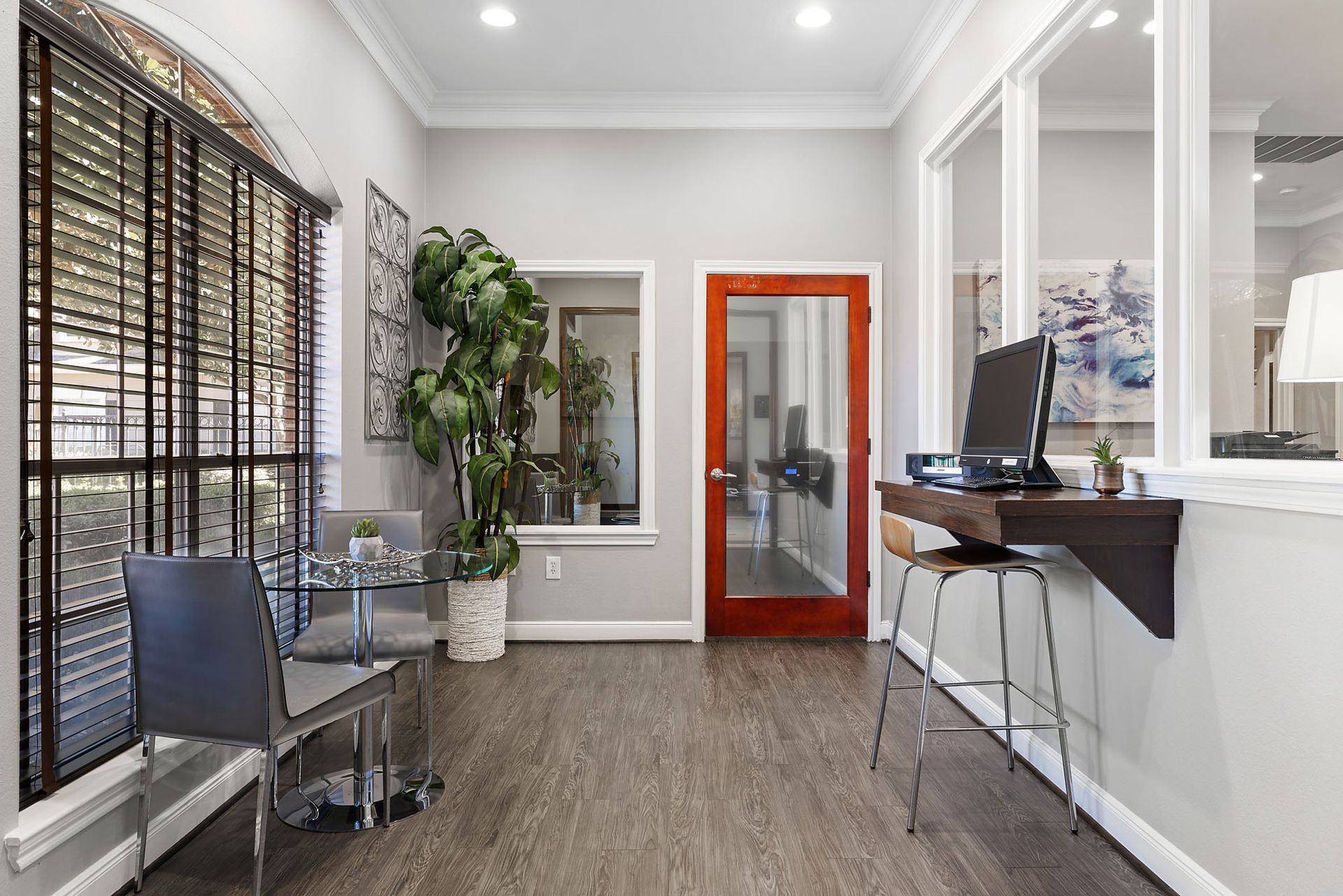 Leasing office area with glass round table, chairs, plant, and computer desk.