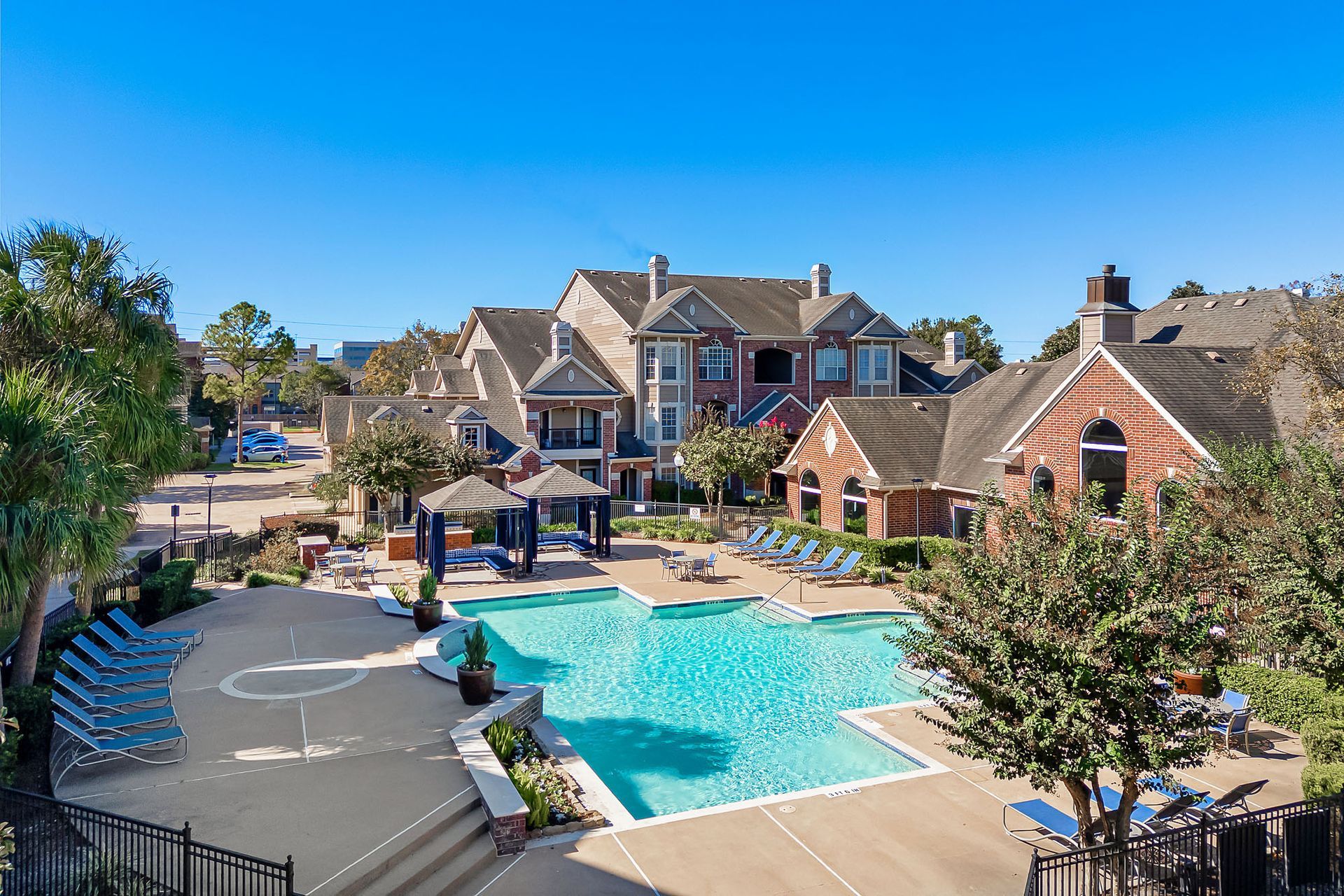 Outdoor pool area with lounge chairs and a cabana among townhouse-style buildings.