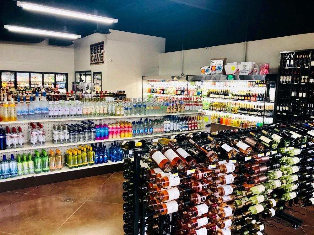 Liquor store interior with wine racks, shelves of alcohol bottles, and coolers.