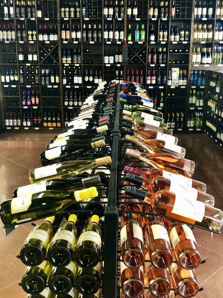 Wine bottles on display in a store, organized on a central rack with shelves of more bottles in the background.