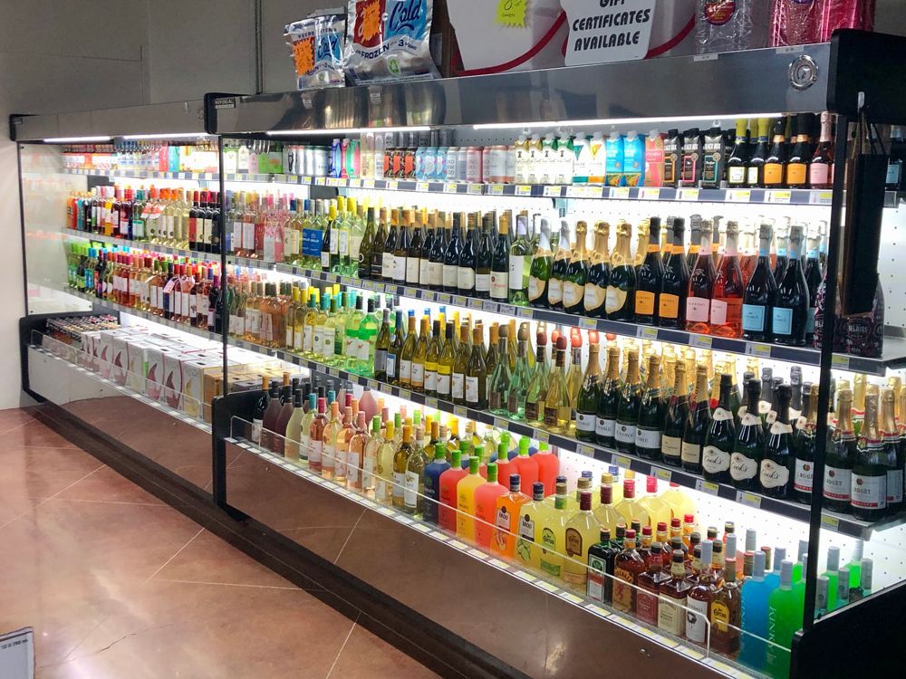 Refrigerated shelves stocked with various alcoholic beverages in a brightly lit store setting.