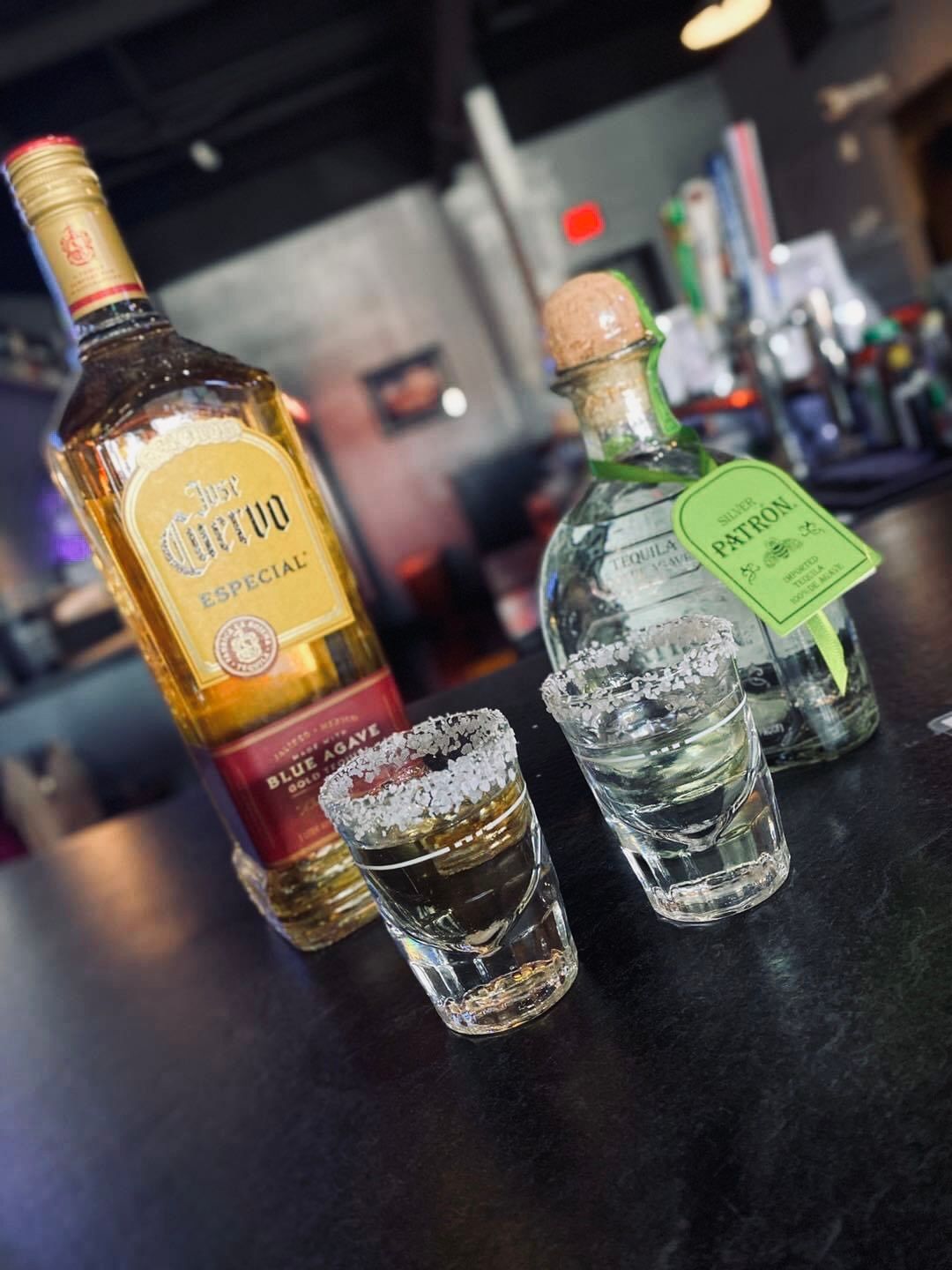 Tequila bottles and shot glasses on a bar, salt on glass rims.