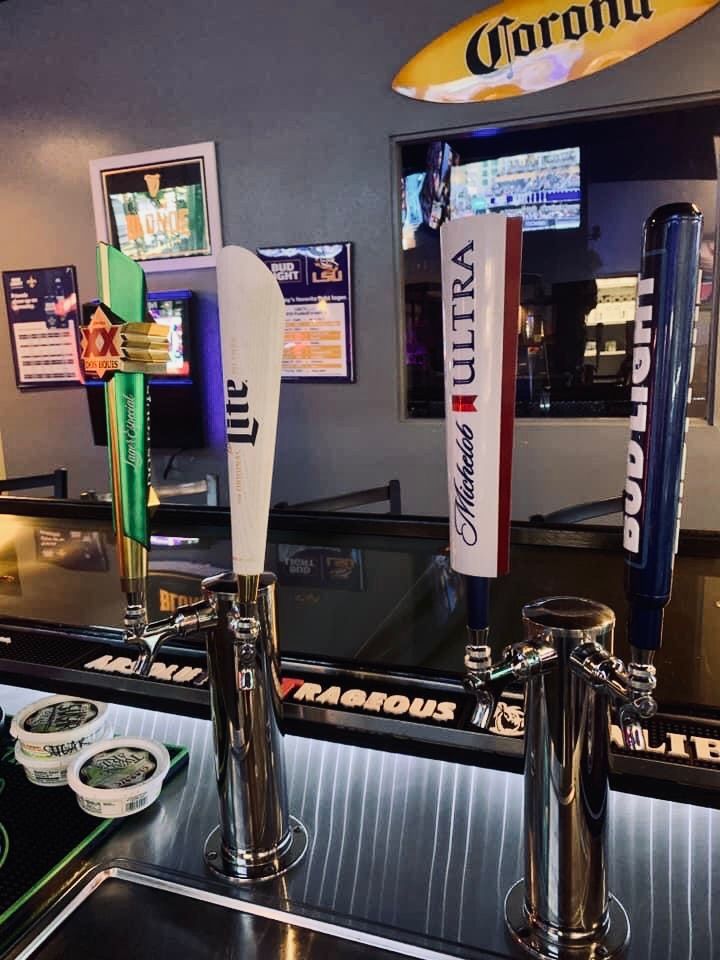 Beer taps at a bar, including Coors Light, Michelob Ultra, and Bud Light, with TVs and Corona sign.