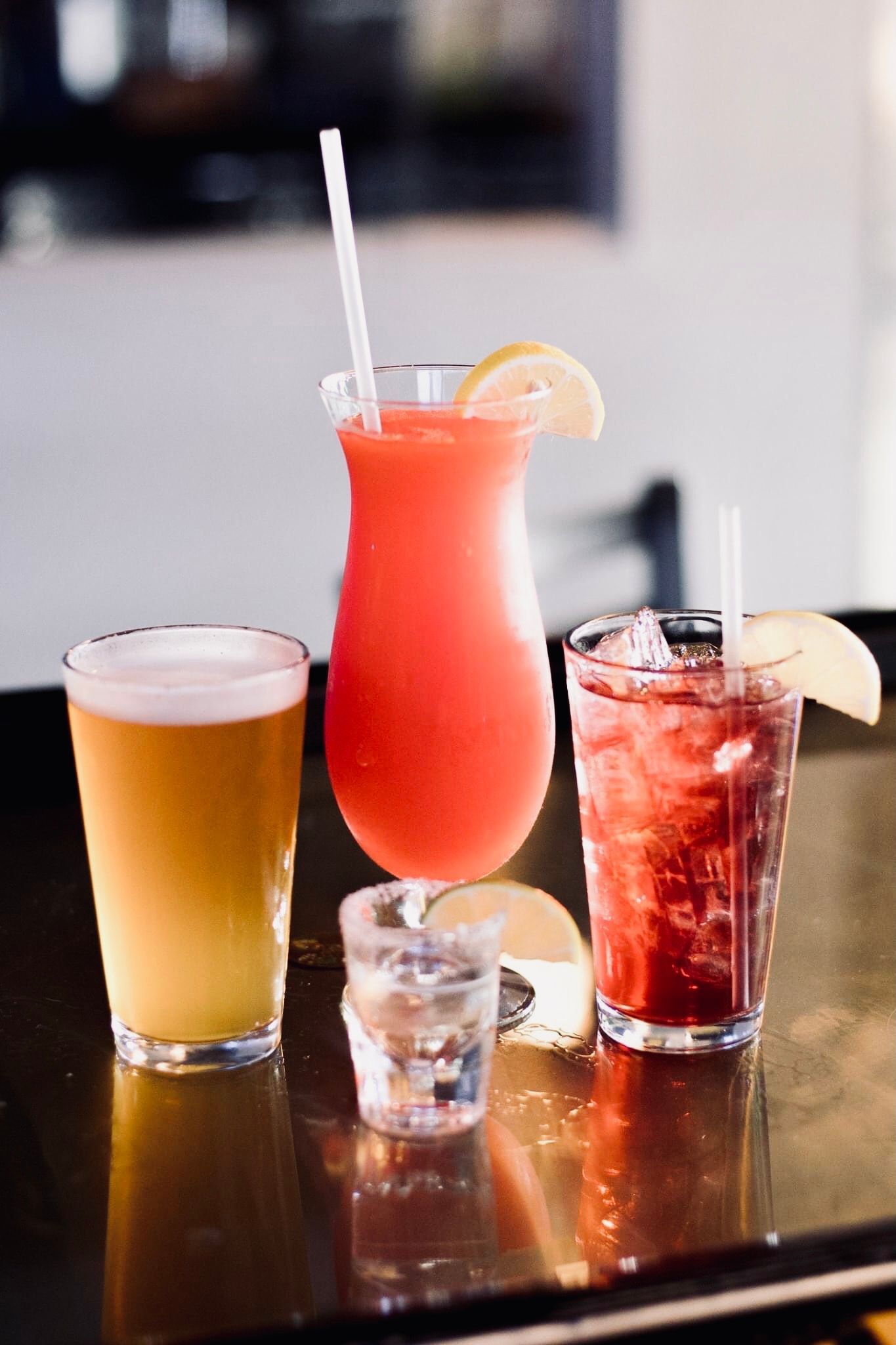 Drinks on a bar: beer, a red cocktail, a red cocktail with ice, and a shot glass.