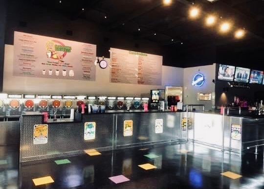 Interior of a frozen drink shop with various flavors available, menus, and a shiny metal bar.