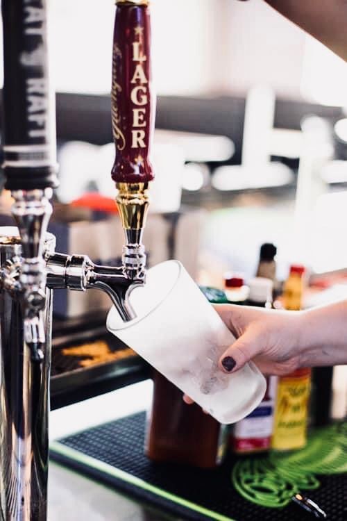 A person pouring lager from a tap into a frosted glass at a bar.