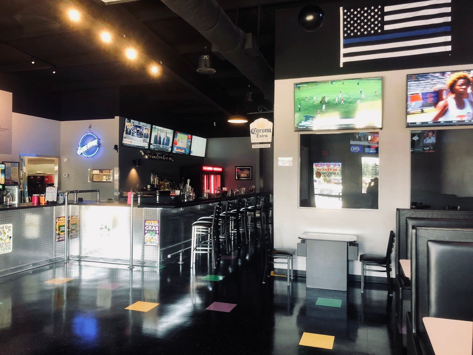 Interior of a sports bar with a bar, tables, TVs, and an American flag with a blue line.