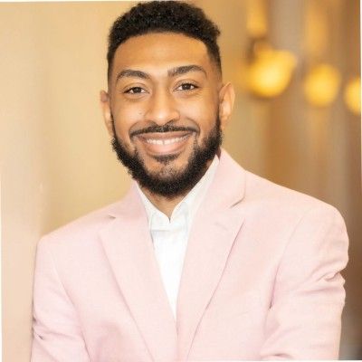 Smiling man in a light pink blazer against a warm, softly blurred background
