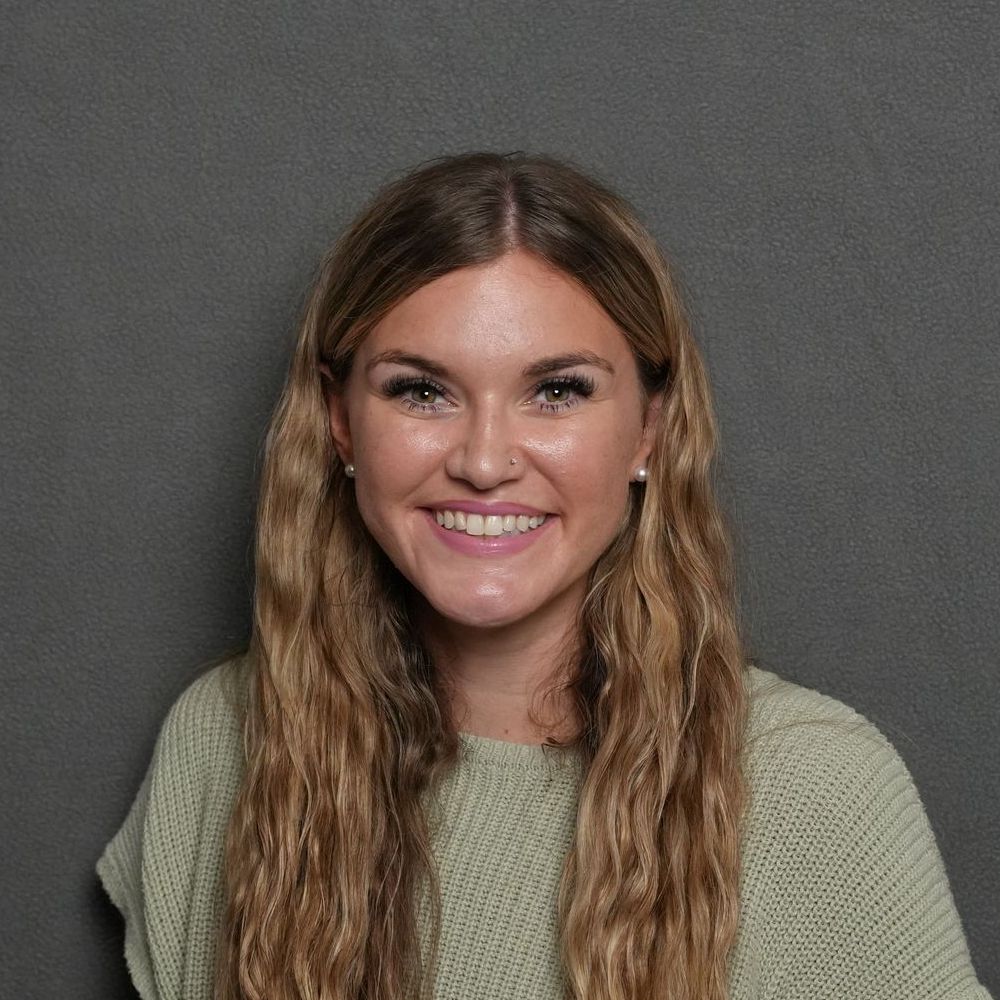 A woman with long hair is smiling and wearing a green sweater.
