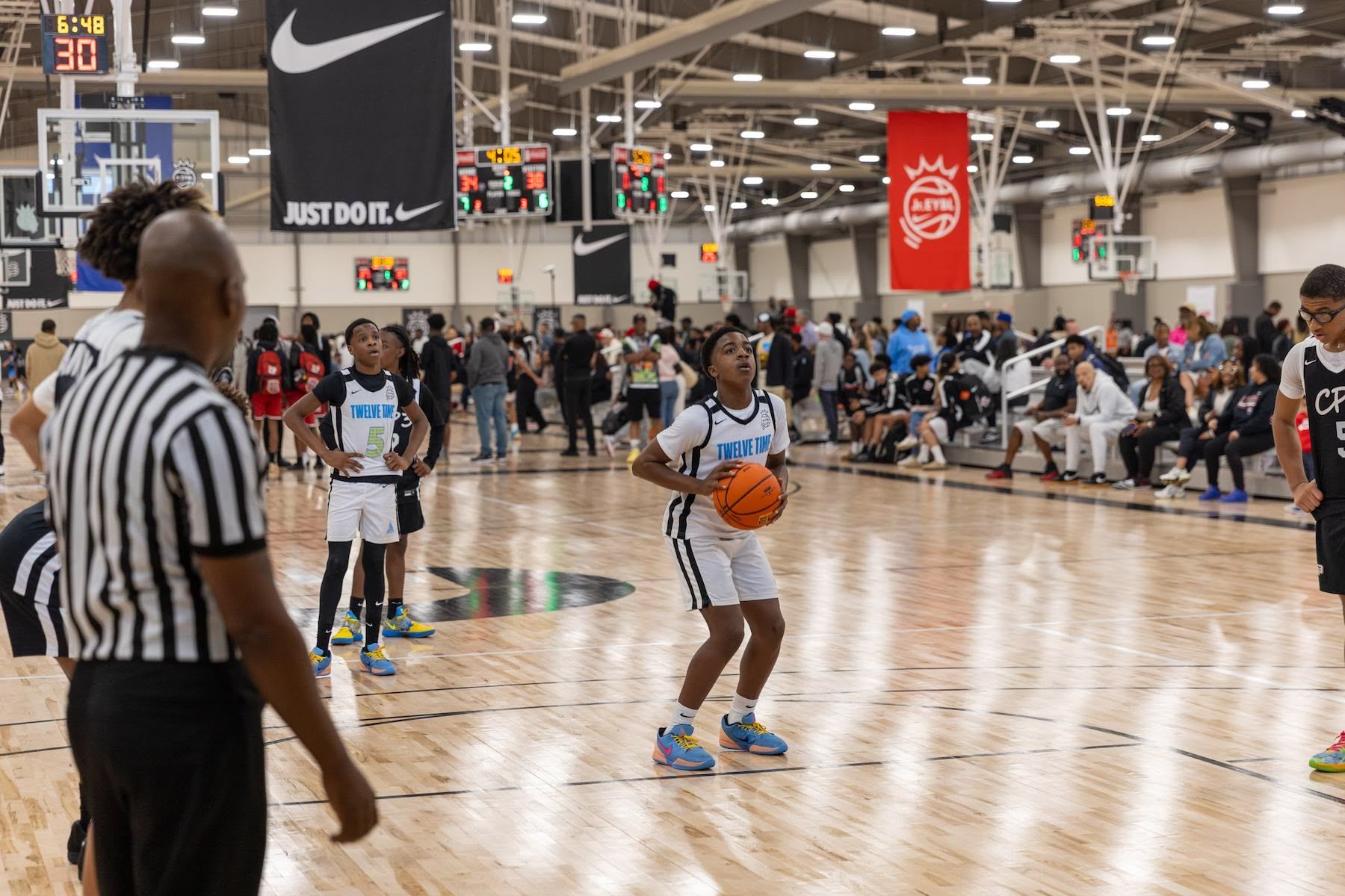 A young basketball player in a blue and white jersey prepares to shoot a free throw during a game in a crowded indoor arena.