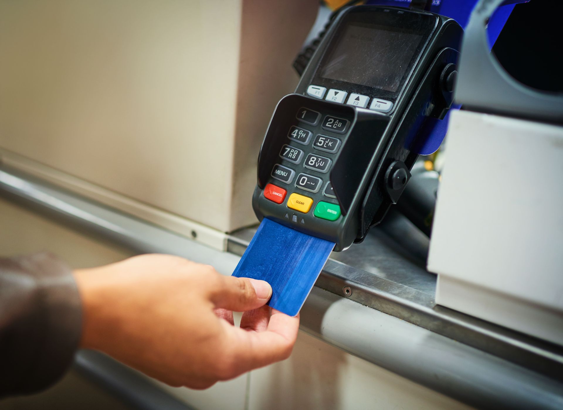 A person is holding a blue credit card in front of a credit card machine.