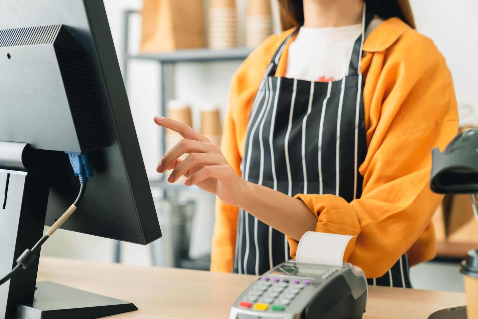 A woman in an apron is standing at a counter in front of a computer.