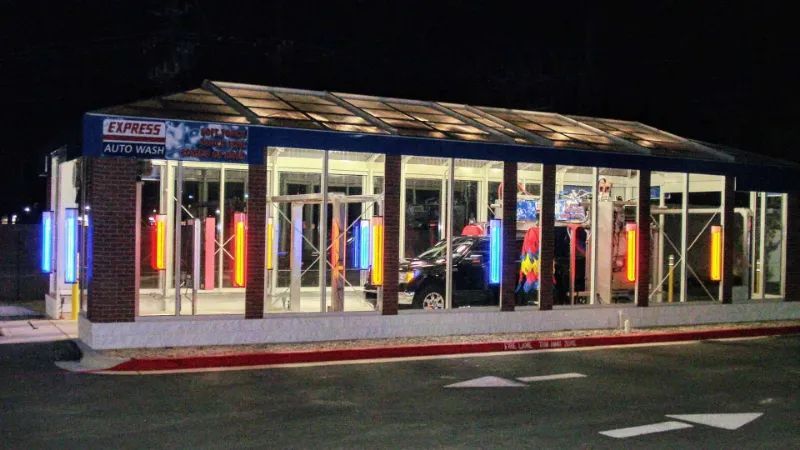 A car wash is lit up at night in a parking lot.