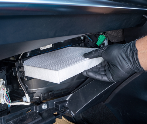 Gloved hand sliding a white cabin air filter into a car dashboard compartment