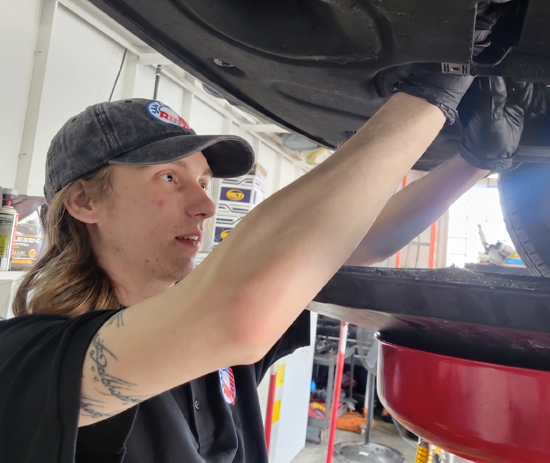 Technician removing the oil drain plug under a lifted vehicle for an oil change.