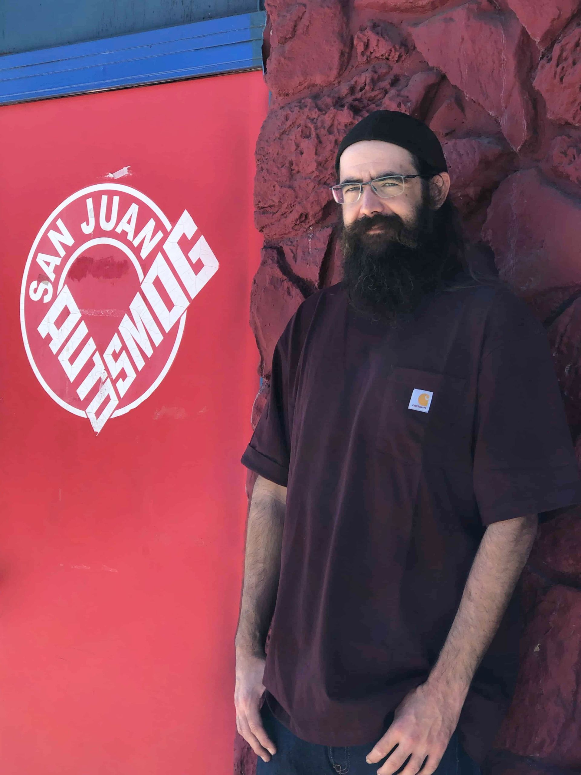 A man with a beard is standing in front of a sign that says san juan splitsmog