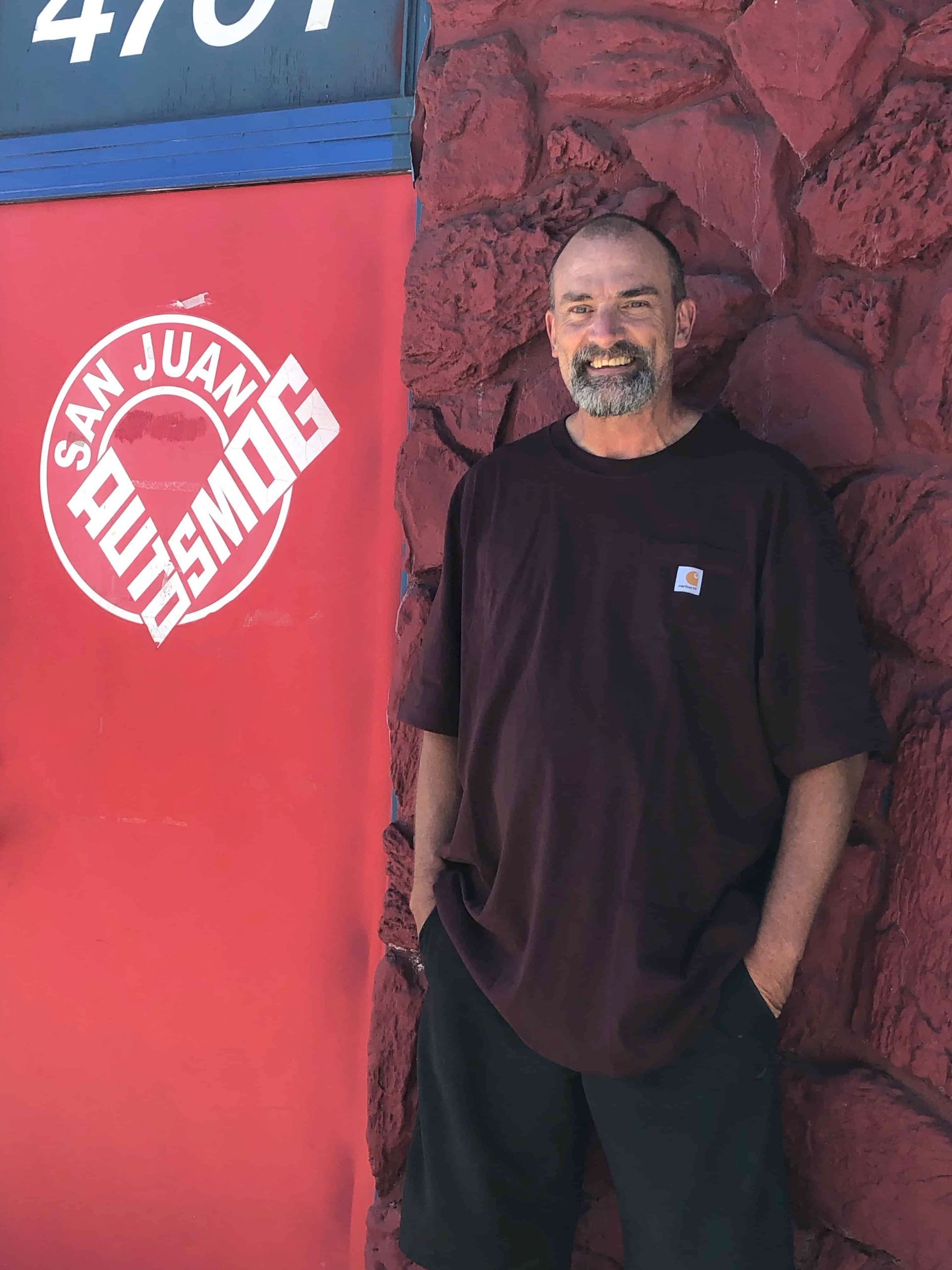A man standing in front of a red wall that says san juan