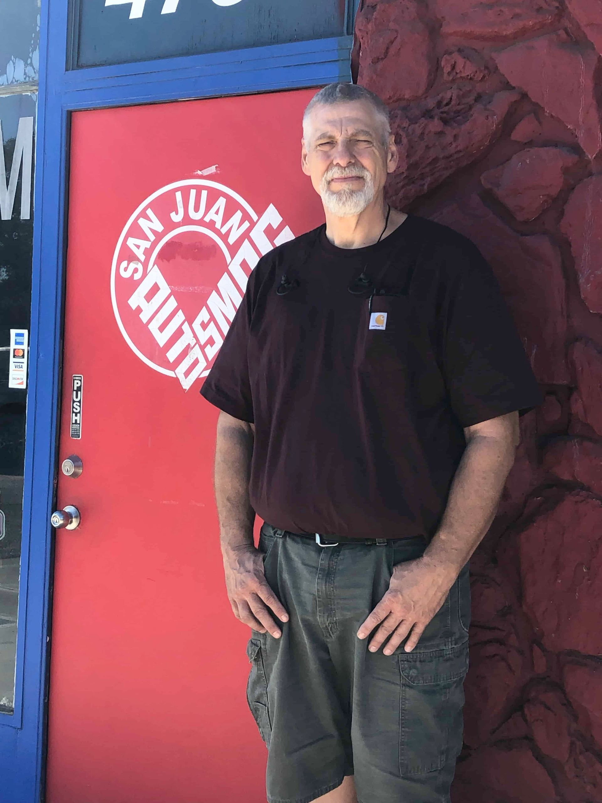 A man standing in front of a red door that says ' san juan ' on it