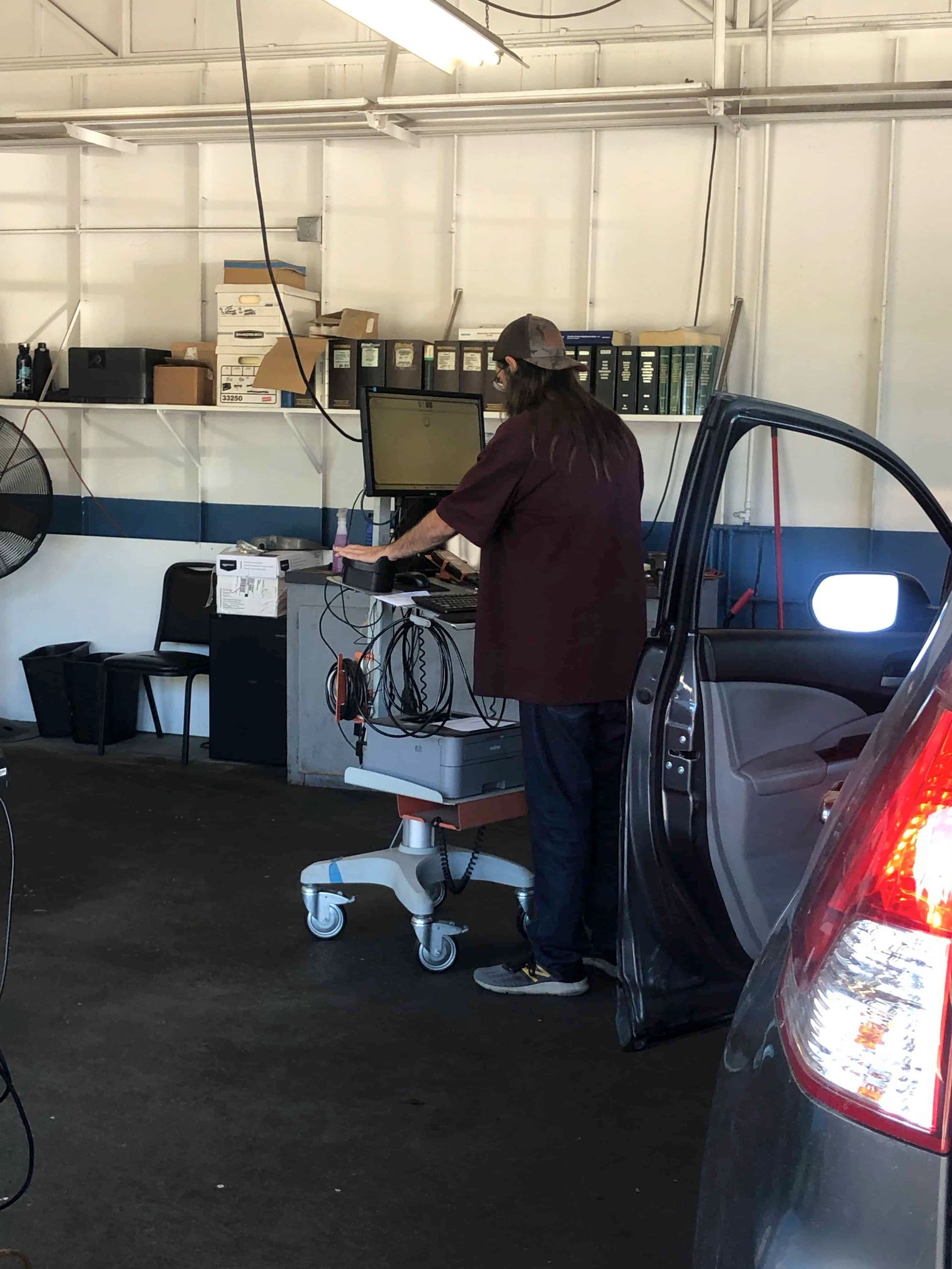 A man is working on a computer in a garage next to a car.