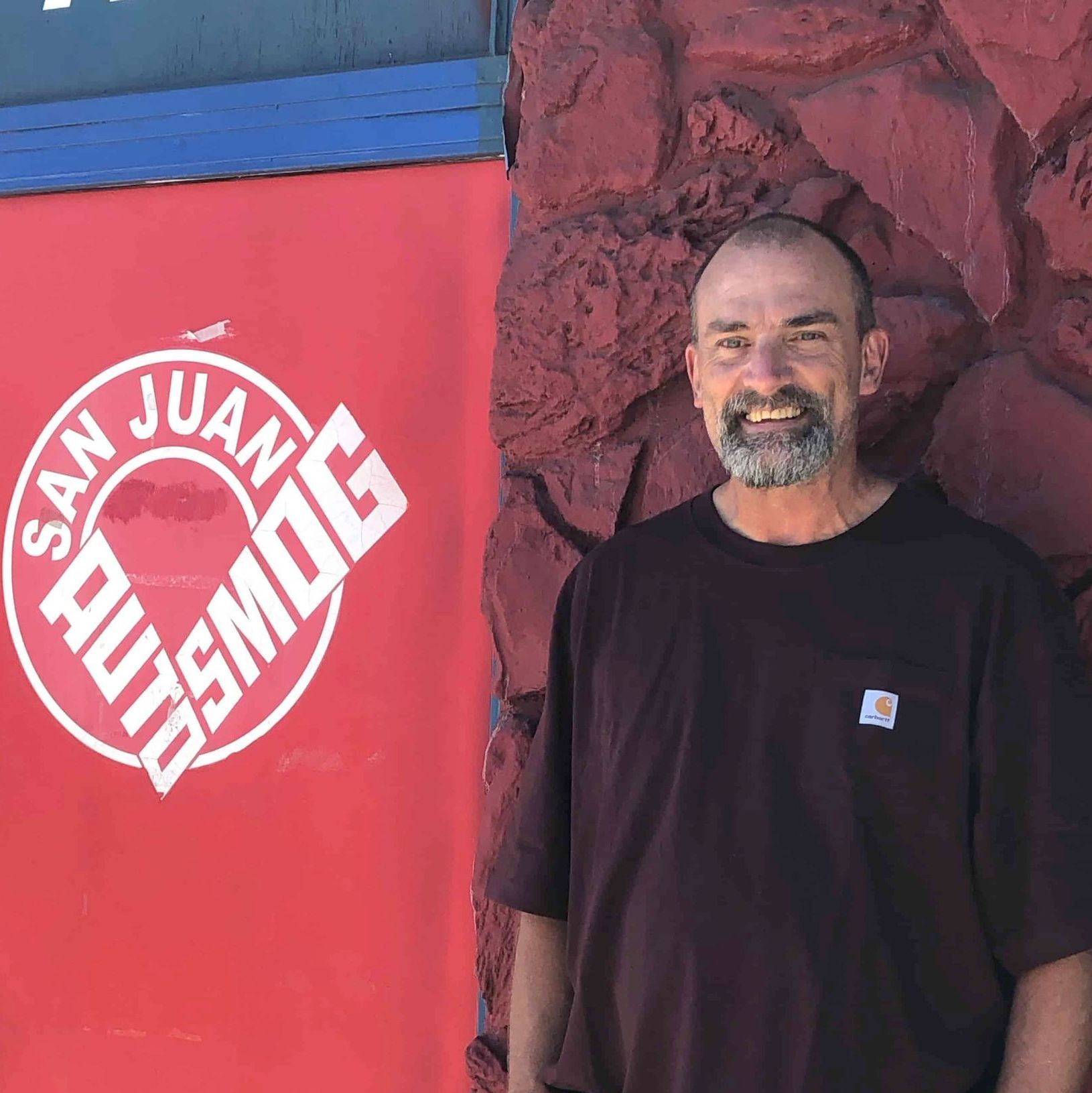 A man stands in front of a sign that says san juan autosmog