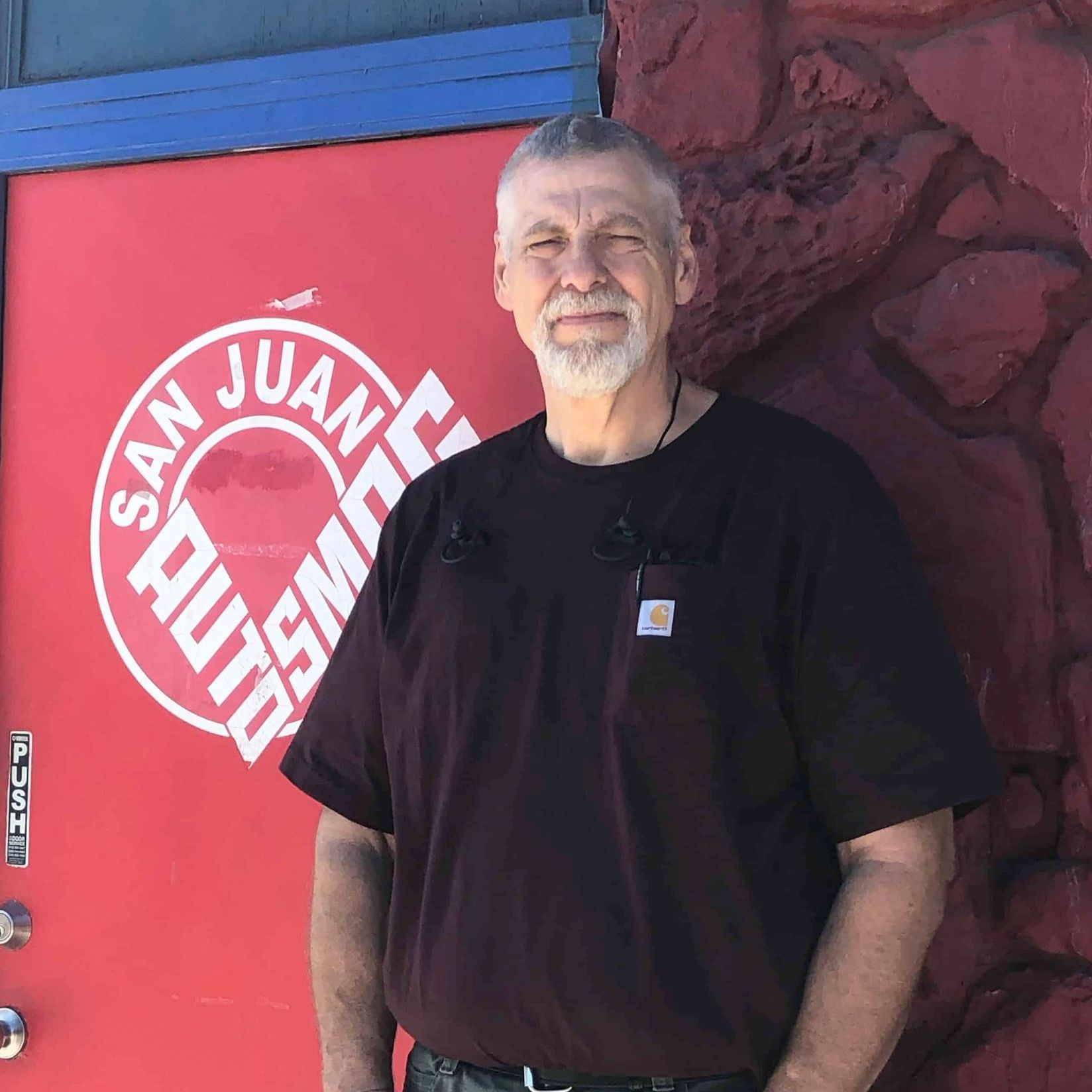 A man standing in front of a red door that says san juan auto