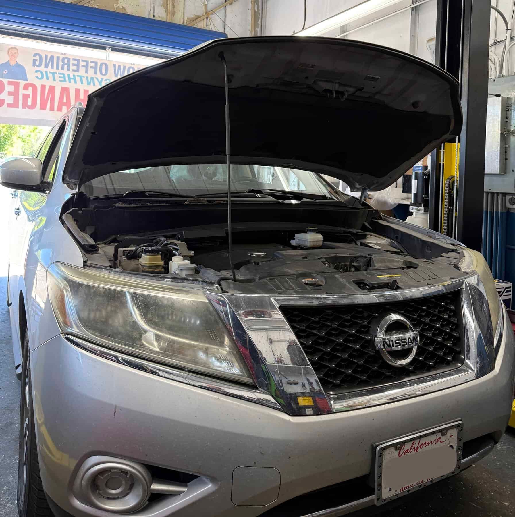 Silver Nissan SUV with hood open in an auto repair shop, front view.