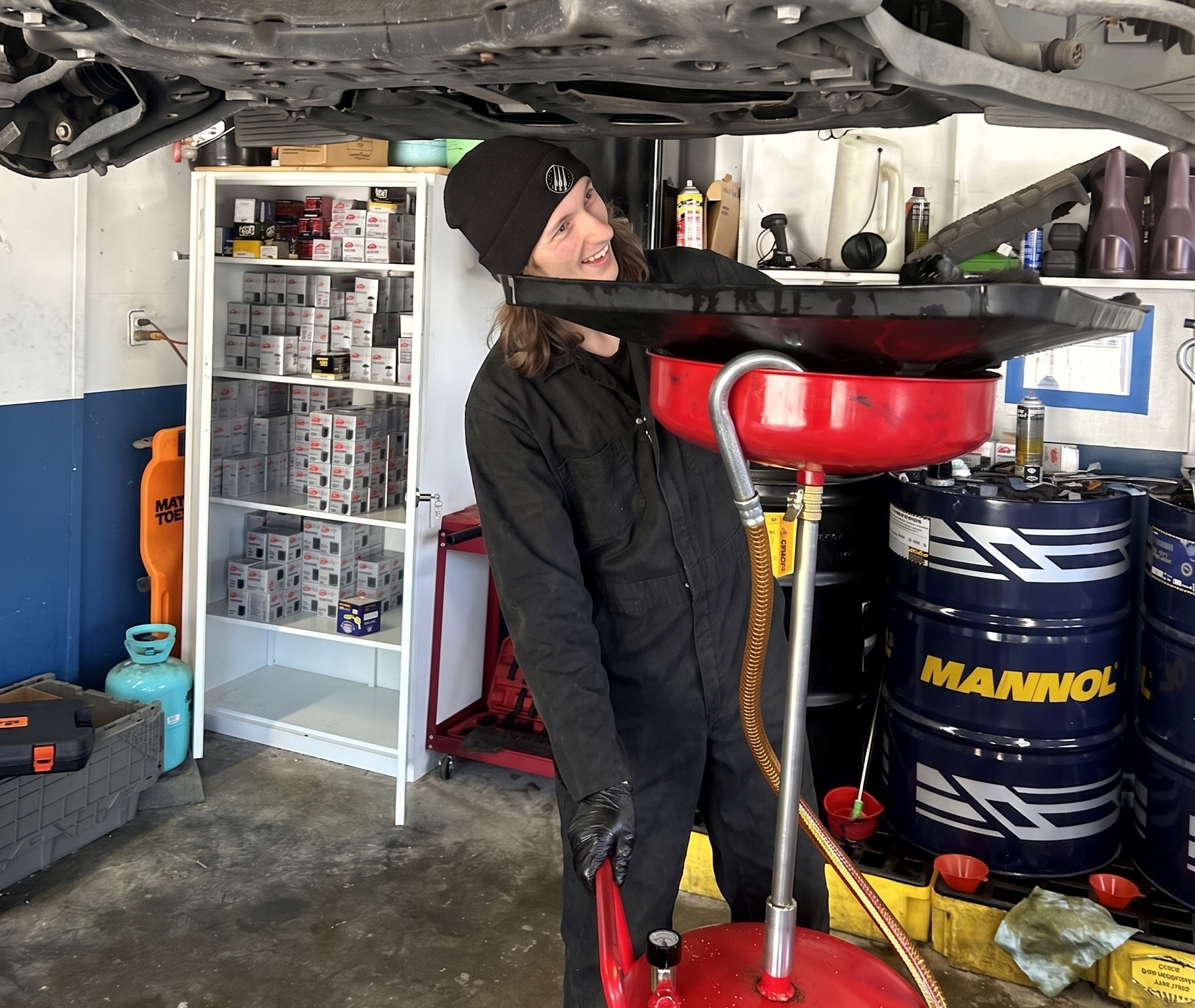 Technician draining engine oil from a vehicle into a catch pan during an oil change.