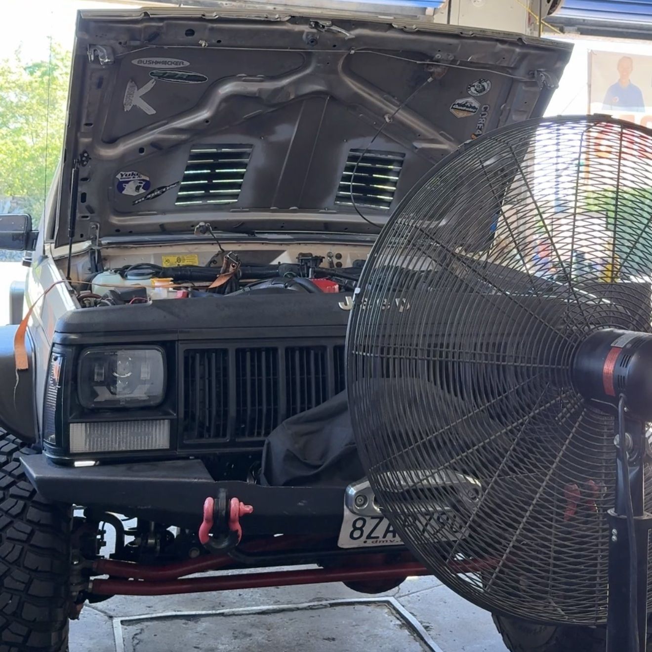 Black off-road vehicle with hood open, red winch, and a large fan in front in a garage or workshop.