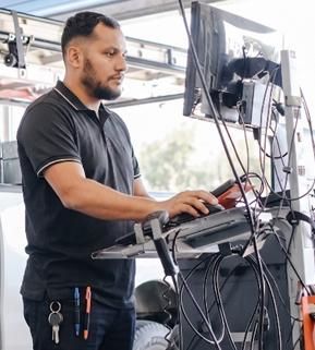 Technician working at a standing workstation with multiple monitors and cables in an industrial setting