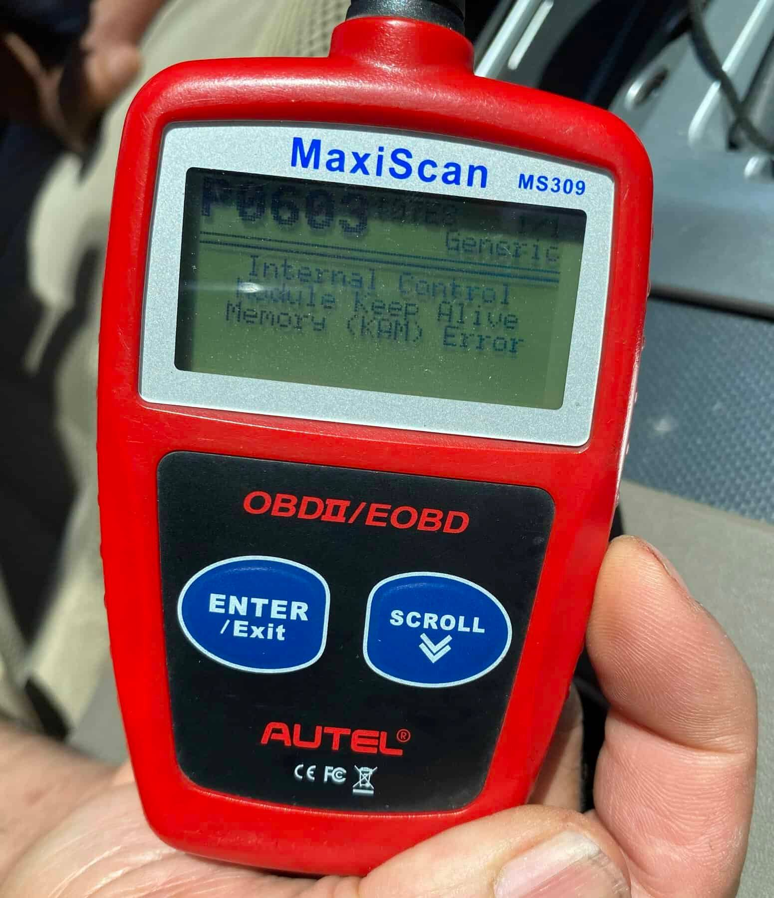 Hand holding a red Autel MaxiScan OBDII/EOBD scanner with a small display screen