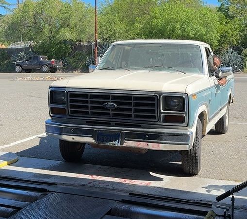 Vintage blue-and-white pickup truck parked in a lot, viewed from the front.