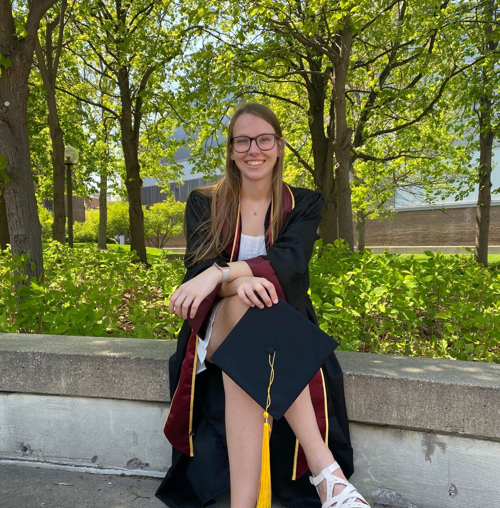 A woman in a graduation cap and gown is sitting on a wall.