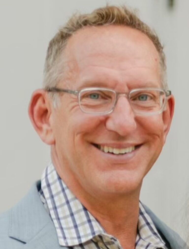 A man wearing glasses and a plaid shirt smiles for the camera
