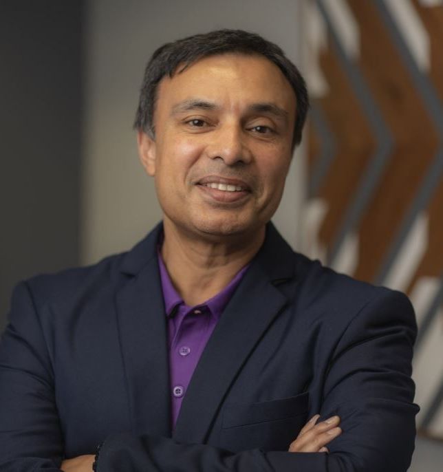 A man in a suit and purple shirt with his arms crossed