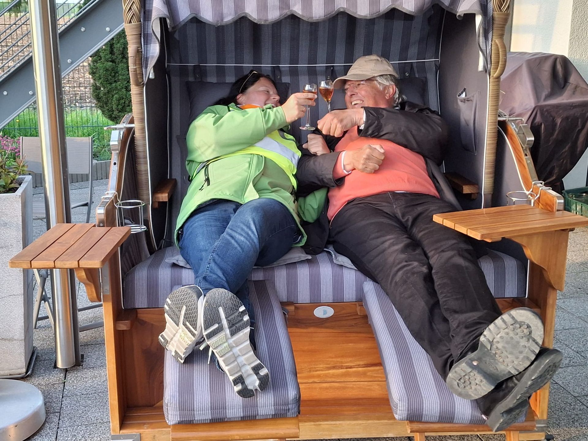 Ein Mann und eine Frau sitzen in einem Strandkorb und stoßen mit Weingläsern an.