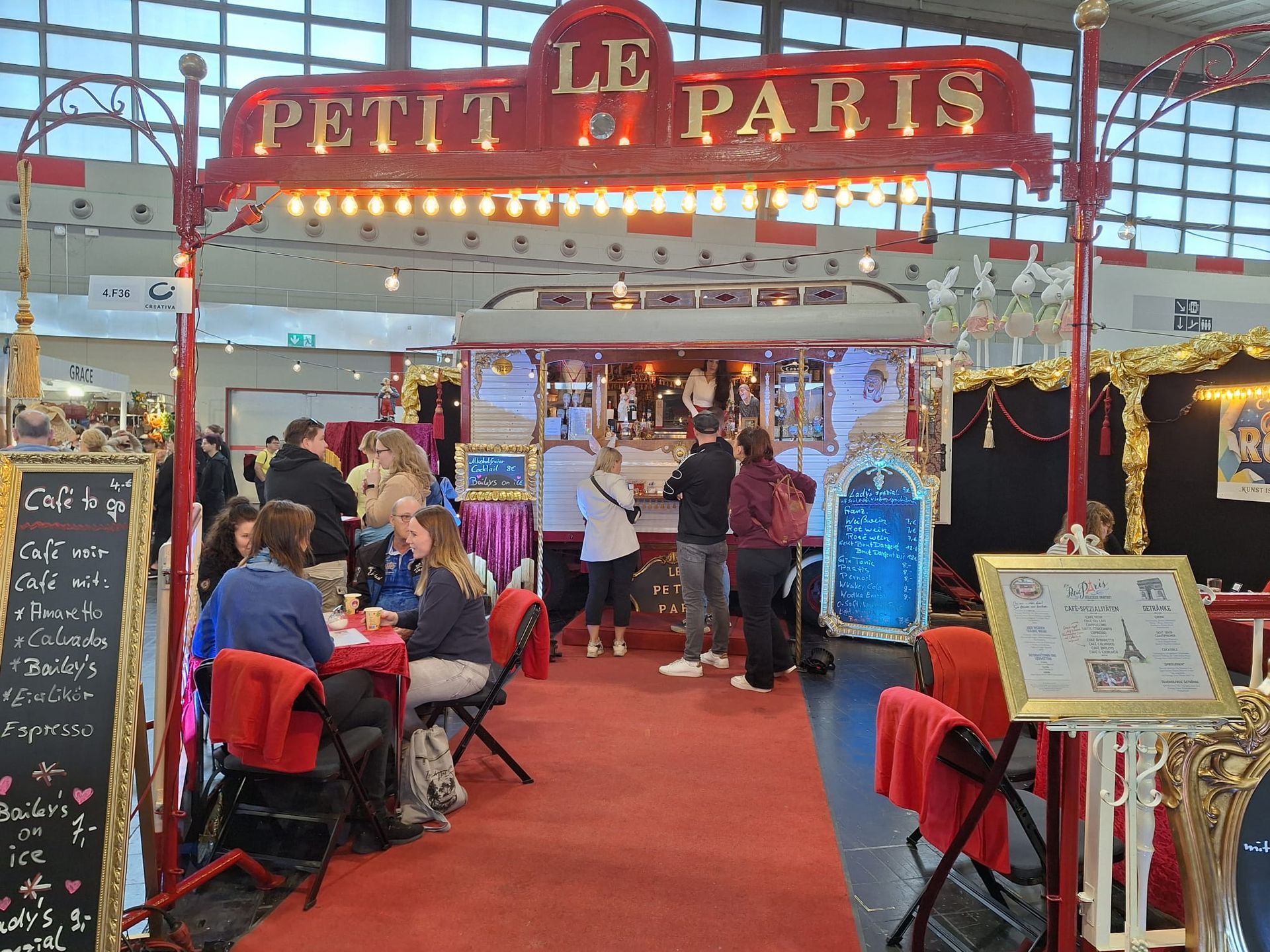 Eine Gruppe von Menschen sitzt an Tischen unter einem Schild mit der Aufschrift „Le Petit Paris“.