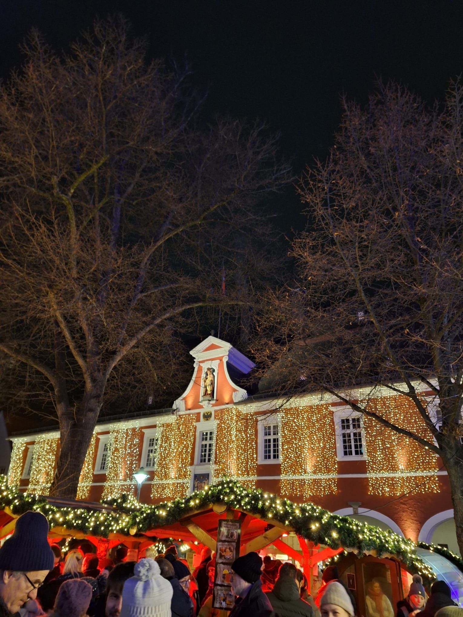 Eine Gruppe von Menschen steht vor einem mit Weihnachtslichtern geschmückten Gebäude.