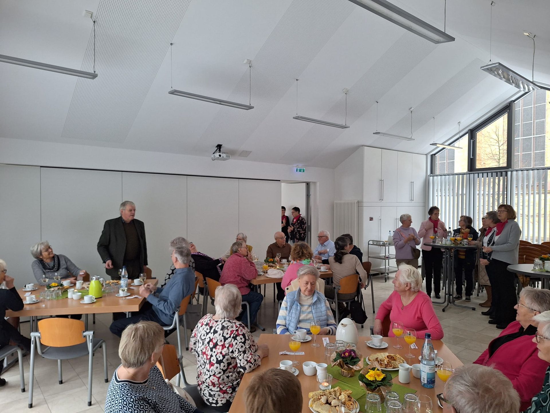 Eine Gruppe von Menschen sitzt in einem großen Raum an Tischen.